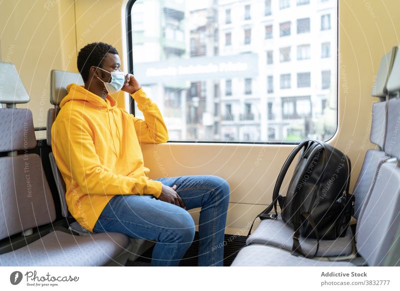 Ethnischer Mann mit medizinischer Maske sitzt in einem modernen Zug Passagier Reisender Fenster Tourist Lächeln Mundschutz neue Normale Coronavirus männlich