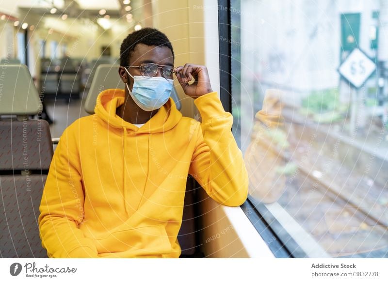 Ethnischer Mann mit medizinischer Maske sitzt in einem modernen Zug Passagier Reisender Fenster Tourist Mundschutz neue Normale Coronavirus männlich ethnisch