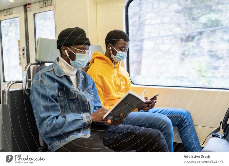 Schwarze Männer fahren während der Coronavirus-Pandemie im Zug Mitfahrgelegenheit Passagier Reisender Zusammensein lesen Buch zuhören Musik ethnisch schwarz