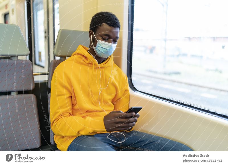 Reisender schwarzer Mann benutzt Handy im Zug Passagier Smartphone neue Normale reisen Mundschutz Coronavirus Eisenbahn ethnisch Afroamerikaner Tourist Sitz