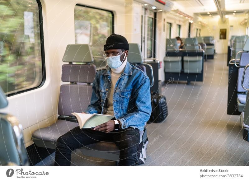 Schwarzer Mann mit Maske liest Buch im Zug lesen reisen Passagier Sitz Eisenbahn Coronavirus männlich ethnisch schwarz Afroamerikaner unterhalten Mundschutz