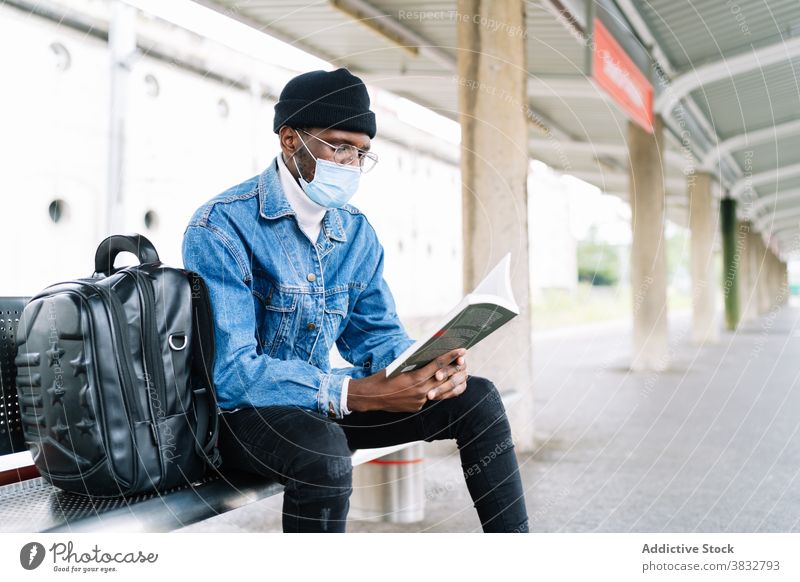 Ethnischer Mann liest Buch auf dem Bahnhof warten Zug Podest lesen Reisender Mundschutz Coronavirus Eisenbahn männlich ethnisch schwarz Afroamerikaner Ausflug