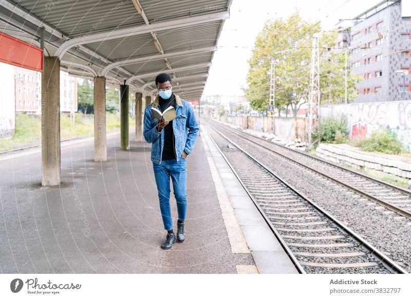 Schwarzer Mann mit Buch auf Bahnsteig warten Zug Eisenbahn Podest neue Normale Reisender Coronavirus Mundschutz männlich ethnisch schwarz Afroamerikaner