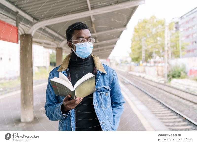 Schwarzer Mann mit Buch auf Bahnsteig warten Zug Eisenbahn Podest neue Normale Reisender Coronavirus Mundschutz männlich ethnisch schwarz Afroamerikaner