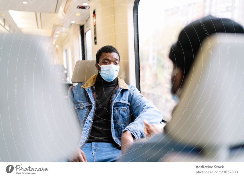 Männliche Freunde fahren im Zug während der Coronavirus-Pandemie Mitfahrgelegenheit Passagier Männer reisen neue Normale Fenster Mundschutz Eisenbahn ethnisch