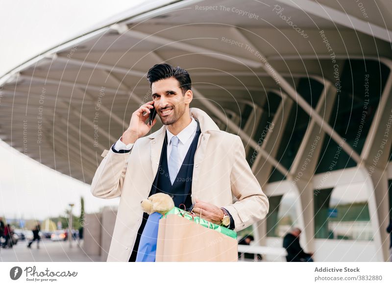 Mann mit Einkaufstaschen telefoniert in der Nähe eines modernen Gebäudes positiv heiter froh formal Geschäftsmann Anruf Telefon männlich ethnisch Schwarzes Haar