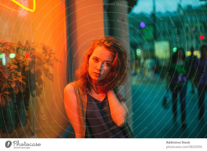 Trendy junge Frau steht in Neonlichter auf der Straße der Stadt sinnlich urban neonfarbig leuchten Nachtleben Dämmerung Licht rote Haare tausendjährig