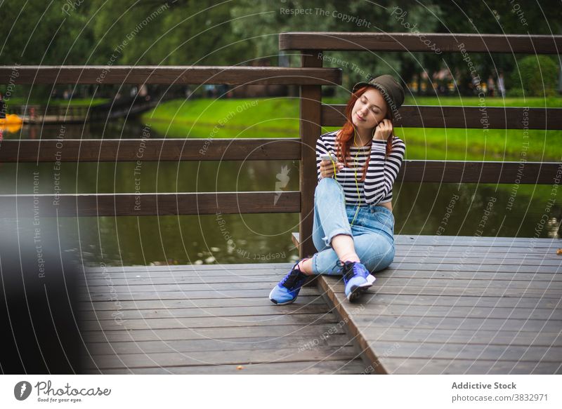 Fröhlicher Teenager beim Musikhören im Park Frau zuhören Kälte Hipster sich[Akk] entspannen ruhen Smartphone Kopfhörer sorgenfrei Stil jung Schüler Sommer