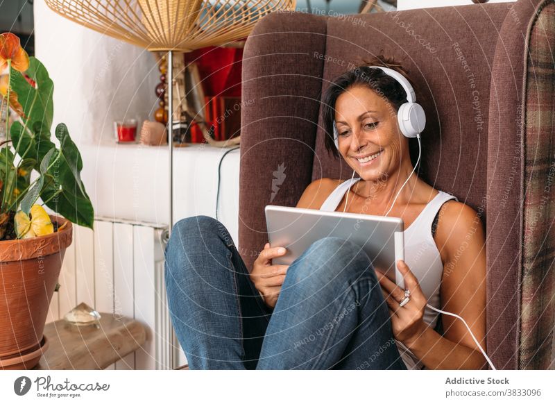 Entspannte Frau mit Tablet und Kopfhörer chillen zu Hause sich[Akk] entspannen Tablette zuhören Stuhl ruhig Musik Erwachsener ethnisch gemütlich Apparatur Gerät