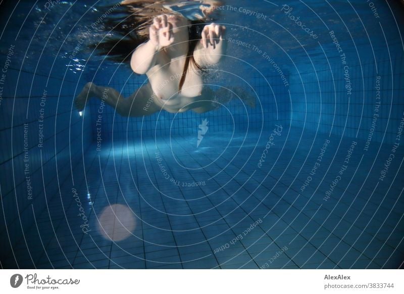 Unterwasser- Körperportrait mit Reflexion an der Wasserlinie von einer jungen Frau die der Kamera entgegen schwimmt junge Frau blass unter Wasser unterwasser
