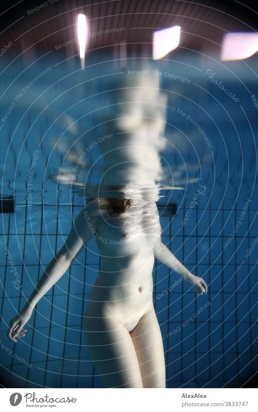 Unterwasser- Körperportrait mit Reflexion an der Wasserlinie einer jungen Frau unter Wasser, die nackt in einem Pool steht und badet junge Frau blass