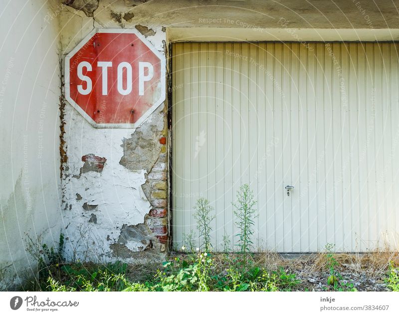 Stopschild neben Garagentor Farbfoto Außenaufnahme Menschenleer Hinterhof Schild Straßenschild Rot Weiß Alt Verfallen Mauer Putz Abgeplatzt Deplatziert