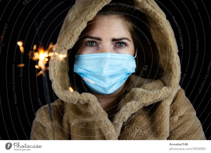 Frohes neues Jahr, Porträt einer jungen Frau, die eine medizinische Maske trägt und für Covid-19, Coronavirus und das Neujahrskonzept Wunderkerzen Licht im Dunkeln hält