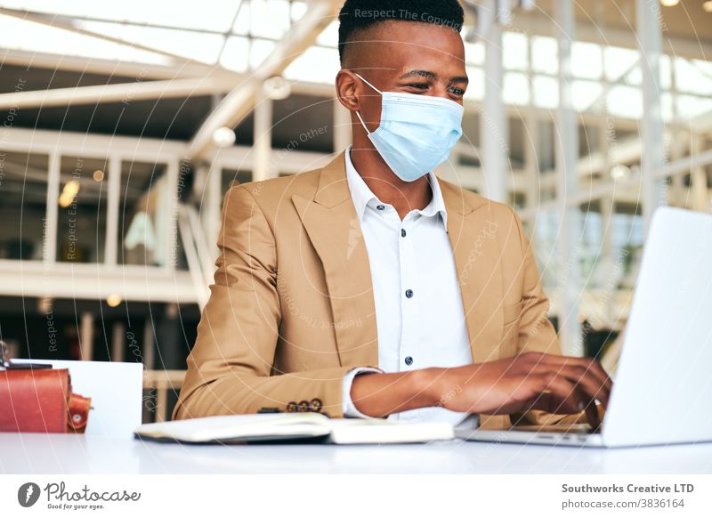Junger Geschäftsmann mit Maske, der während einer Gesundheitspandemie am Laptop am heißen Schreibtisch im Büro arbeitet Business Gesichtsmaske Gesichtsbedeckung