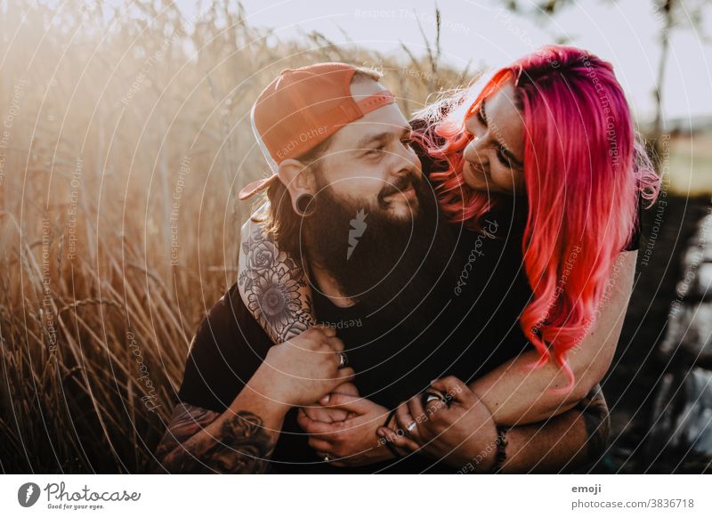 Paar mit Tattoos und pinken Haaren umarmen sich und schauen sich an Frau Mann Hipster trendy kuscheln innig pinke haare kornfeld Draussen paar liebe verliebt