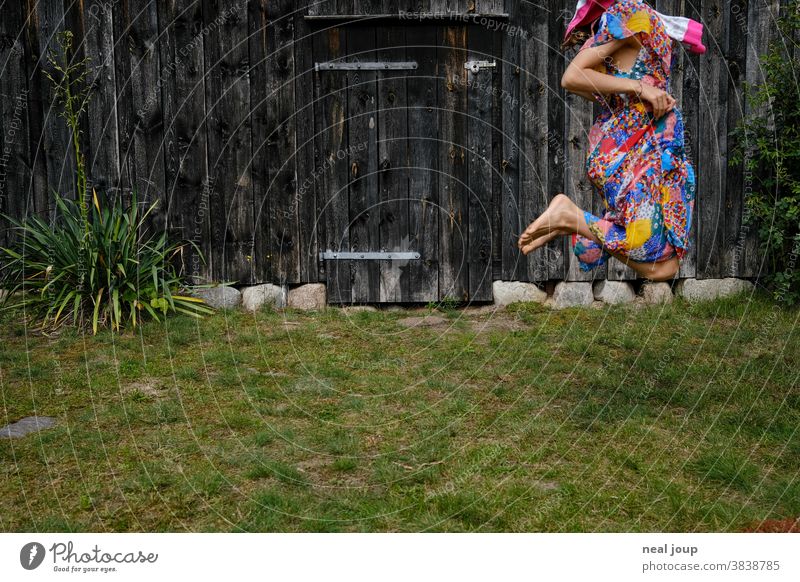 Hüpfendes Kind vor Wand einer alter Scheune hüpfen springen spielen Fröhlichkeit Spaß Spiel Verkleiden bunt Gras Rasen Garten Sommer grün angeschnitten Mädchen