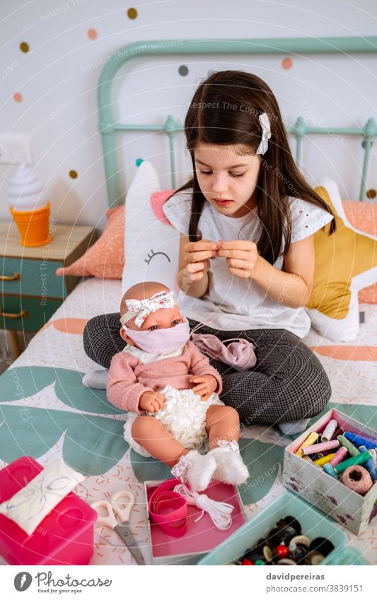Mädchen näht Gesichtsmasken für sich und ihre Babypuppe Spielen Nähen Faser Coronavirus Schutz Nähkästchen Gesundheit Konzept Mundschutz Nadel Covid-Generation