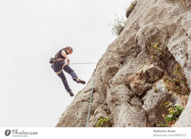 Männlicher Kletterer beim Aufstieg an einer steilen Felswand im Sommer Aufsteiger aufsteigen steile Klippe Mann Alpinist Berge u. Gebirge üben Klettern aktiv
