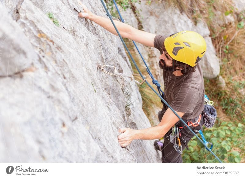 Männlicher Kletterer beim Aufstieg an einer steilen Felswand im Sommer Aufsteiger aufsteigen steile Klippe Mann Alpinist Berge u. Gebirge üben Klettern aktiv