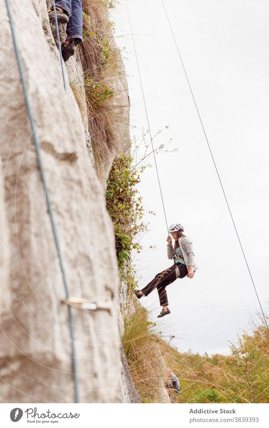 Starke Bergsteigerin in Sicherheitsausrüstung beim Klettern am Felsen an einem sonnigen Tag Frau Seil Gerät Berghang Berge u. Gebirge stark Sportbekleidung