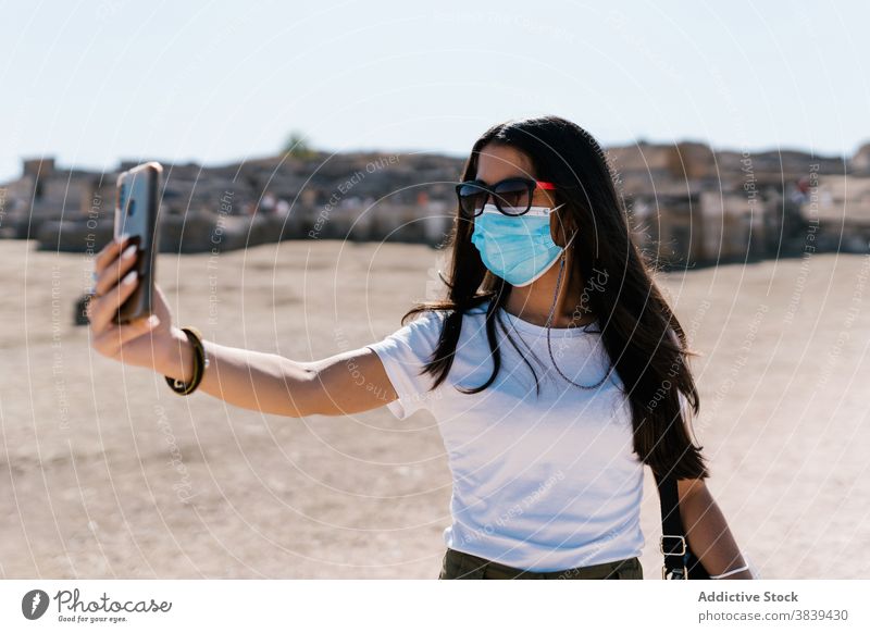 Frau in Maske nimmt Selfie in der Stadt Selbstportrait Smartphone Mundschutz Coronavirus Bund 19 Seuche benutzend fotografieren sonnig Straße jung medizinisch