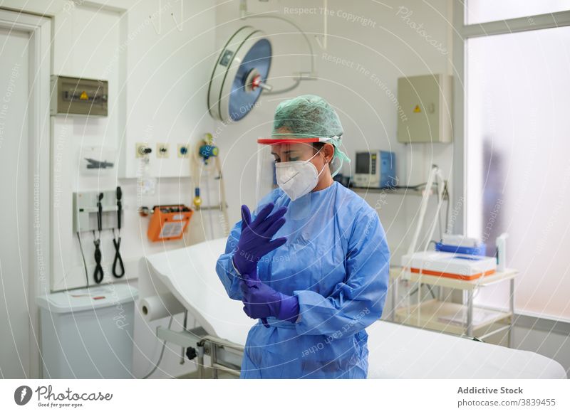 Anonymer Arzt in Uniform zieht sterile Handschuhe an angezogen Job Prozess Gerät medizinisch Klinik Frau Sanitäter Mundschutz Atemwegserkrankungen Krankenhaus
