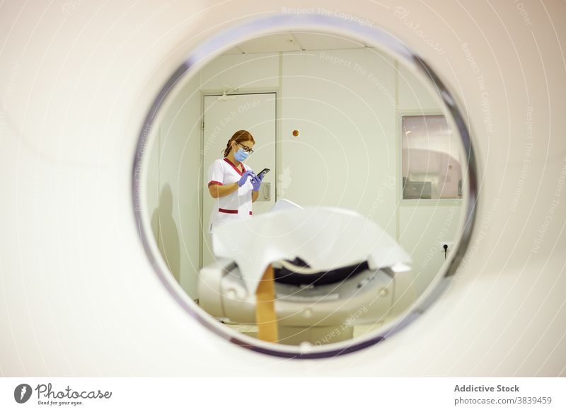 Anonymer Sanitäter in Uniform surft bei der Arbeit mit dem Smartphone im Internet Fenster Surfen Gerät Frau Klinik benutzend Arzt Mundschutz schützend Liege