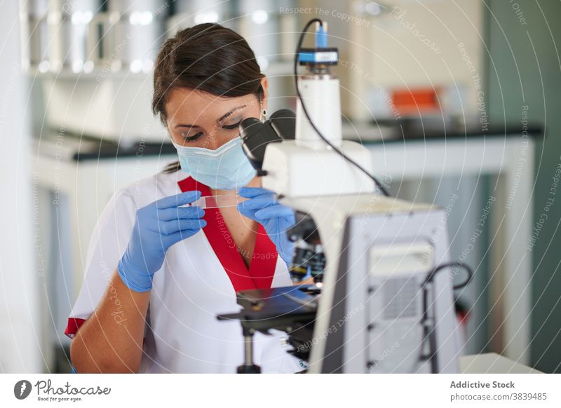 Wissenschaftlerin mit Glasprobe in der Nähe des Mikroskops im Labor Spezialist medizinisch Probe Uniform steril Beruf Gerät Frau professionell Metall Material