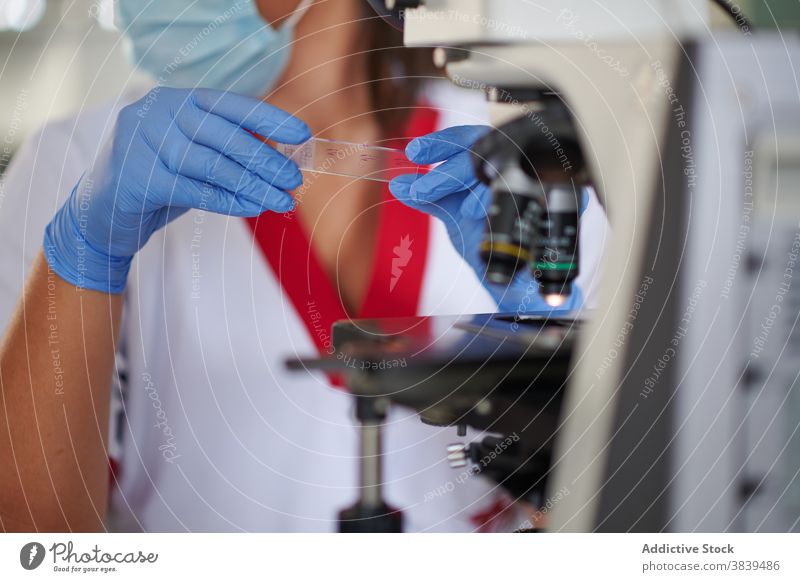 Anonymer Wissenschaftler mit Glasprobe in der Nähe des Mikroskops im Labor Spezialist medizinisch Probe Uniform steril Beruf Gerät Frau professionell Metall