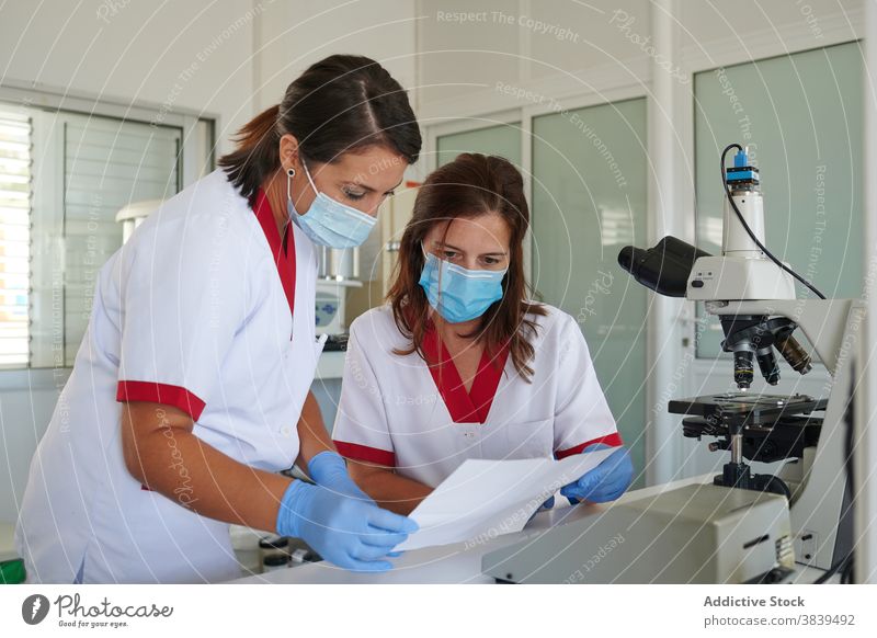 Anonyme Medizintechniker beobachten Papier in der Nähe des Mikroskops im Labor Wissenschaftler zuschauend Uniform Fokus medizinisch Kollege Frauen Partner