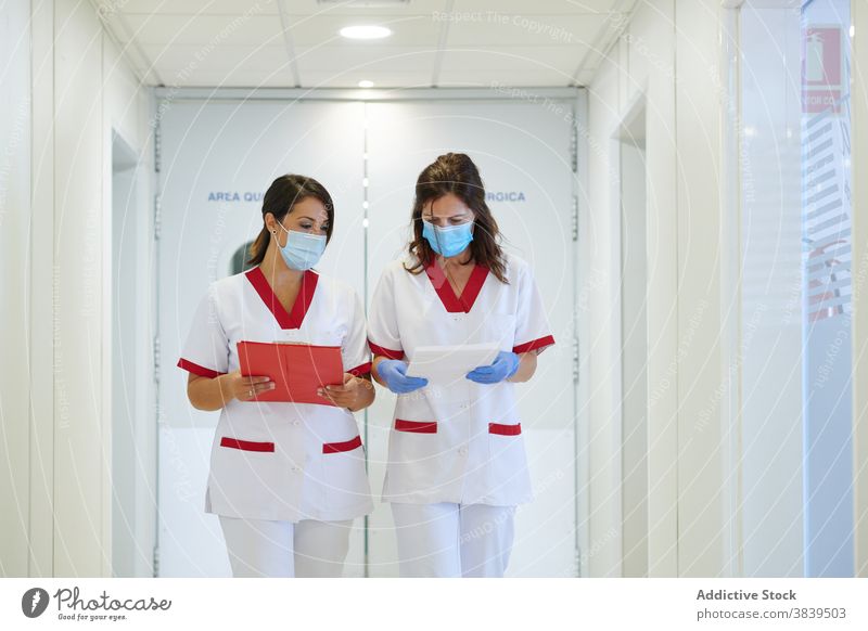 Anonyme Krankenschwestern in Uniformen mit Papieren interagieren in der Krankenhauspassage medizinisch Personal Beruf Spaziergang Durchgang Frauen