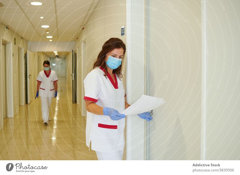 Anonyme Krankenschwester in Uniform mit Papieren interagiert in der Krankenhauspassage medizinisch Personal interagieren Beruf Spaziergang Durchgang Frauen