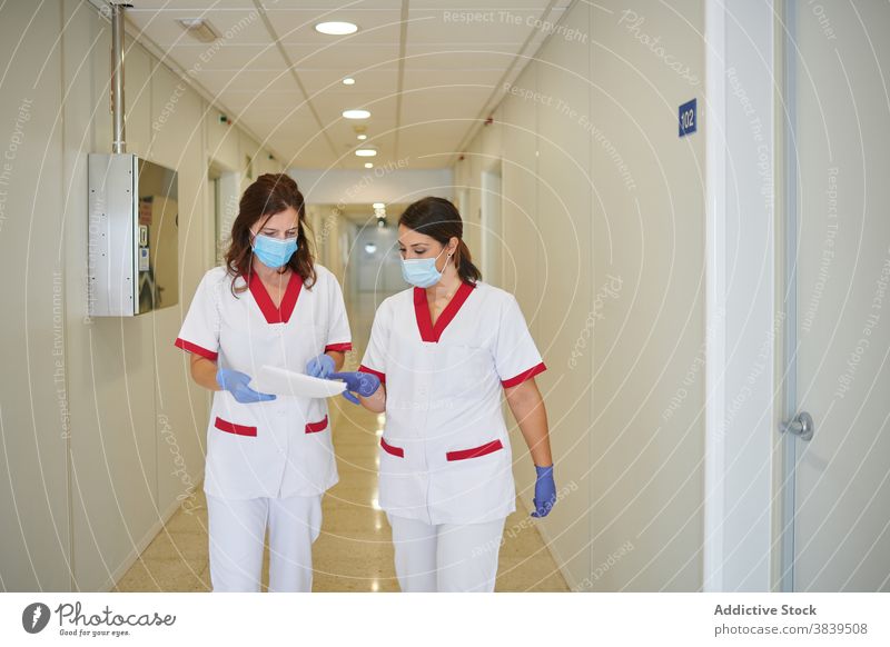 Anonyme Krankenschwestern in Uniformen mit Papieren interagieren in der Krankenhauspassage medizinisch Personal Beruf Spaziergang Durchgang Frauen