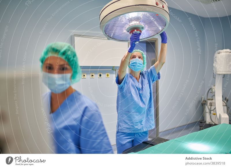 Anonymer Arzt, der eine Lampe in der Nähe eines Kollegen bei der Arbeit einstellt ausrichten Mitarbeiterin Uniform professionell Gerät medizinisch Frauen Klinik