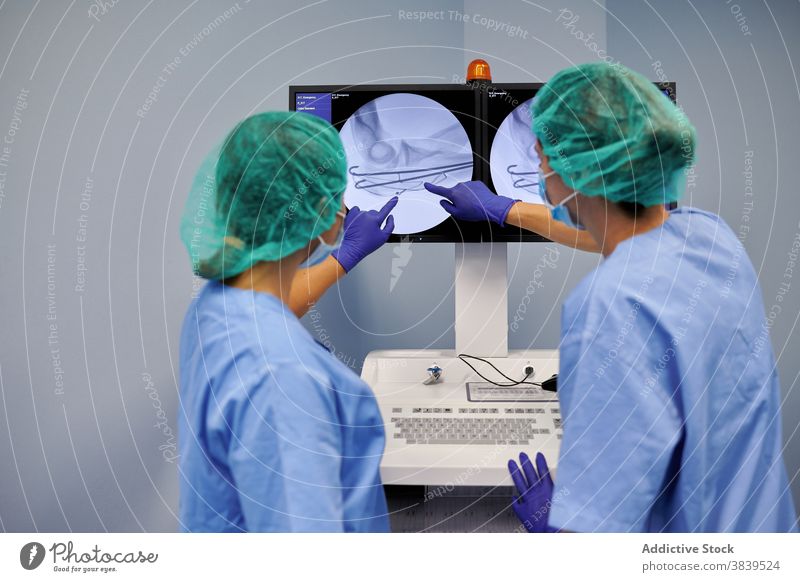 Unkenntlich gemachte Ärzte, die bei der Arbeit auf den Monitor eines Diagnosegeräts zeigen Sanitäter Punkt Gerät Diagnostik Anzeige Bild medizinisch Uniform
