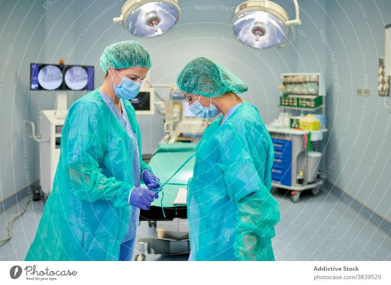 Anonymer Arzt, der einem Kollegen beim Anziehen der OP-Kleidung in der Klinik hilft angezogen Uniform Hilfsbereitschaft Krawatte chirurgisch Beruf Frauen
