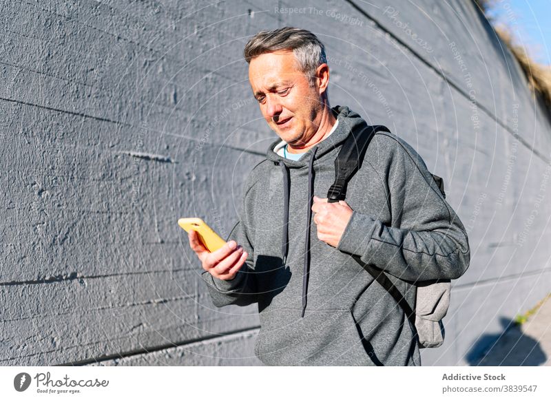 Senior im Ruhestand Mann mit Sportkleidung und Smartphone zu Fuß die Straße hinunter 60 ruhen Rhythmus Gesundheitswesen Fitness Training kardial alt Hals Pflege