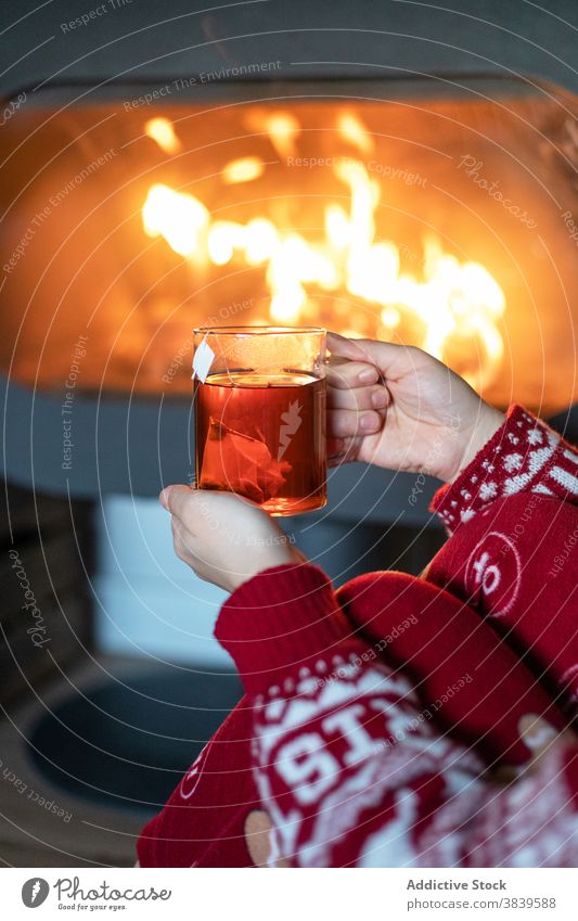 Crop Frau mit Tasse Tee in der Nähe von Kamin Feuerstelle Weihnachten gemütlich warm Atmosphäre Schornstein Feiertag Nacht rot Neujahr Pullover