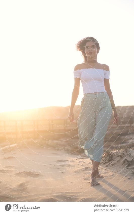 Serene Frau zu Fuß auf Sandstrand bei Sonnenuntergang sorgenfrei Sommer Spaziergang Strand Barfuß Anmut ruhig Outfit Hügel Natur charmant genießen Freiheit jung