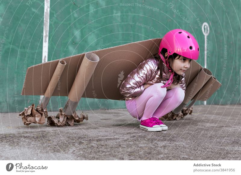 Nettes Mädchen in handgemachten Karton Flügel und Helm auf der Straße Kind Jetpack spielen Schachtel handgefertigt niedlich wenig Ebene Schutzhelm behüten