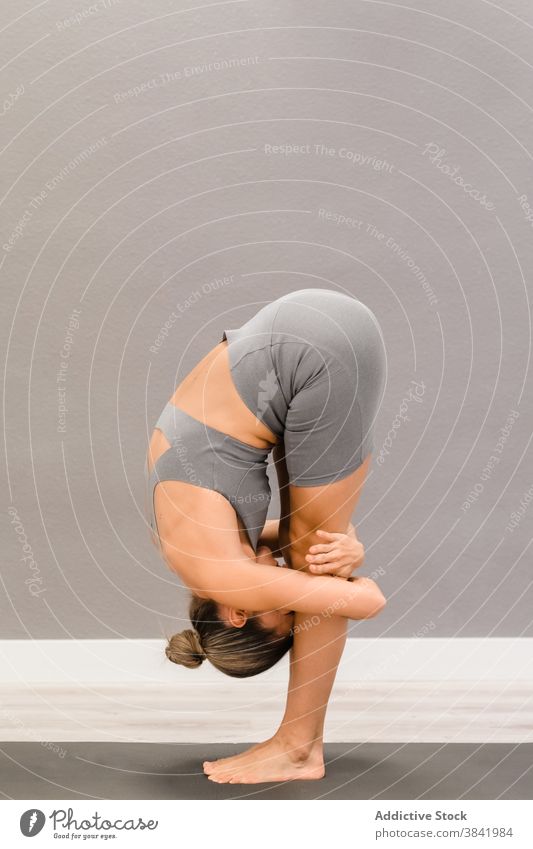 Flexible Frau stehend in Vorwärtsbeuge auf Yogamatte Asana Dehnung beweglich Unterlage uttanasana üben Barfuß Sportbekleidung passen schlank friedlich