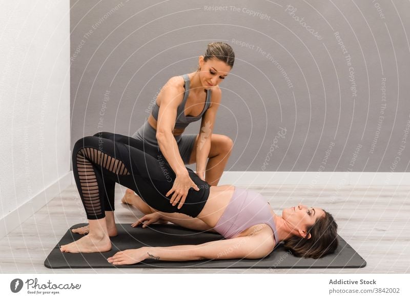 Schlanke Frau macht Yoga mit Trainer im Studio Klasse Ausbilderin Frauen Hilfsbereitschaft abstützen Brückenstellung beweglich üben Pose professionell