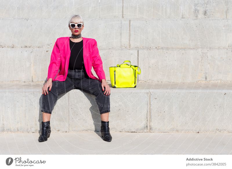 Stilvolle kreative Frau in rosa Jacke in der Stadt lebhaft Outfit Model Großstadt trendy Farbe hell gelb Handtasche Stoff Straße sitzen cool urban pulsierend