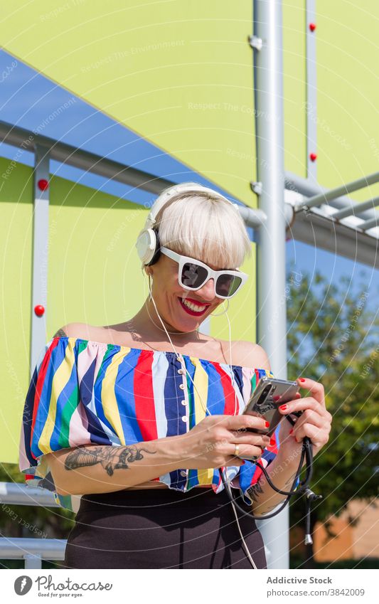 Positive Frau, die mit Kopfhörern Musik hört zuhören Stil Straße farbenfroh Hipster Erwachsener Smartphone Gesang Outfit trendy Sonnenbrille Klang Audio modern