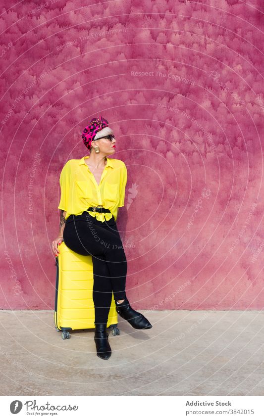 Trendy Frau sitzt auf gelben Koffer in der Stadt hell Farbe Outfit Reisender Tourist lebhaft Großstadt Gebäude rosa Wand Tasche Gepäck Ausflug reisen Stil