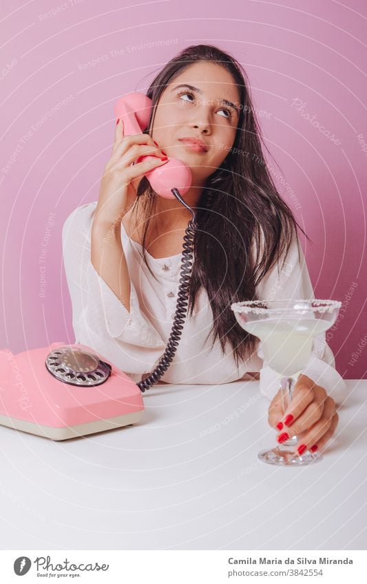 Fröhliche und lächelnde junge brünette Frau mit Getränk, benutzt ein altmodisches Telefon. Porträt auf rosa Hintergrund schön Brasilianer Einwegartikel trinken