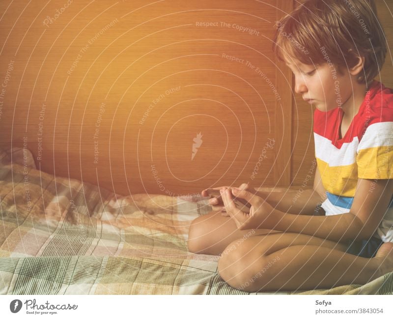 Kleiner blonder Junge spielt Spiele am Smartphone Kind spielen allein Mobile benutzend App Apparatur digital zuschauend Bildschirm Gerät Schule Spaß heimwärts
