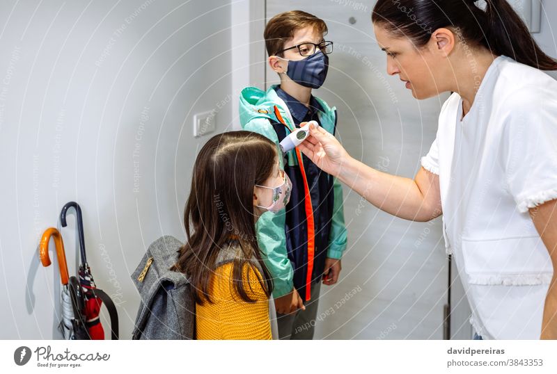 Mutter kontrolliert die Temperatur ihrer Tochter vor dem Schulbesuch Thermometer Überprüfung Fieber Coronavirus Schutzmaske heimwärts Familie im Innenbereich