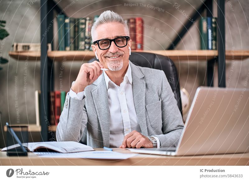 Stilvoller, reifer Geschäftsmann, der in die Kamera schaut und lächelt, während er im Büro arbeitet gutaussehend im Innenbereich Blick Lächeln Drahtlos Laptop