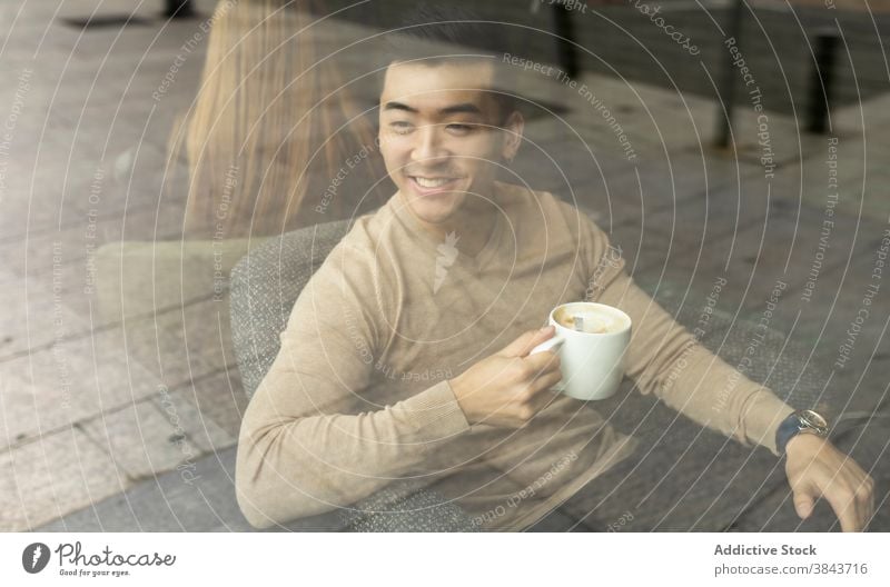 Glücklicher ethnischer Mann trinkt Kaffee im Café trinken sich[Akk] entspannen Wochenende Kaffeehaus Armsessel gemütlich Getränk männlich asiatisch heiß modern